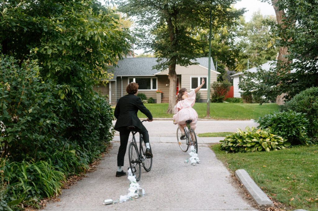 documentary-style wedding photo of bride and groom biking away on wedding day