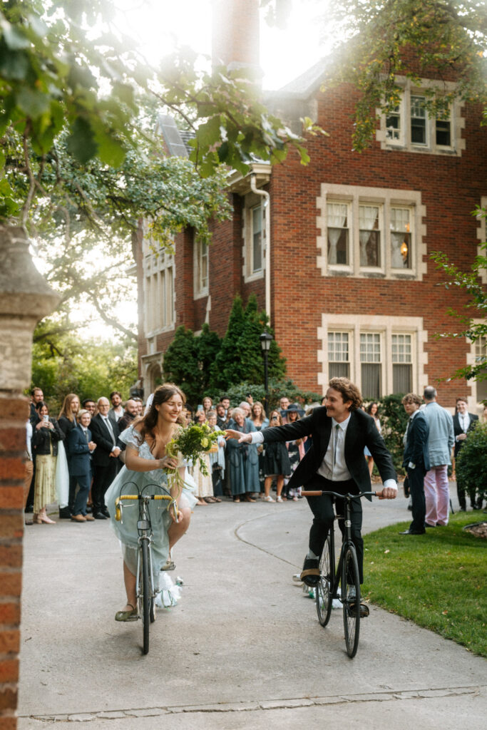 bride and groom bike away from wedding guests